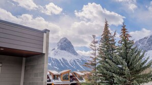 A modern building with a sloped roof, a mountain in the background, and a coniferous tree in the foreground. - Summit View Penthouse in Downtown Canmore at Brookside Lane (Canmore)