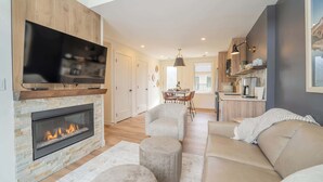 A modern living room with a fireplace, a flat-screen TV, a dining area, and a kitchen. - Summit View Penthouse in Downtown Canmore at Brookside Lane (Canmore)