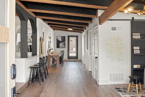 A hallway with wooden beams, a dining area with chairs and a table, and a white wall with a grid pattern. - Modern Pool Retreat Near Dallas & Stadium (Irving)