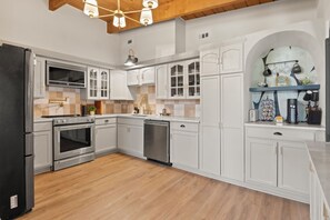 A modern kitchen with white cabinetry, stainless steel appliances, and a wooden floor. - Modern Pool Retreat Near Dallas & Stadium (Irving)