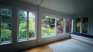 Una habitación con ventanas amplias, piso de madera y alfombra gris.