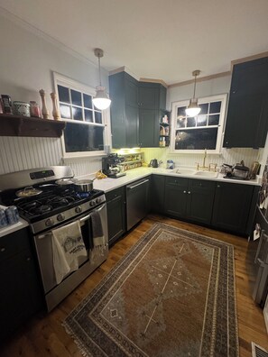 Una cocina con estufa, horno y lavaplatos, piso de madera y armarios verde oscuro.