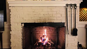Una chimenea encendida, con repisa de ladrillo blanco, un mapa enmarcado encima de la repisa y un estante con diversos objetos.