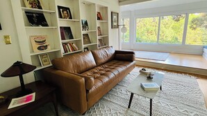 Una sala de estar con un sofá de cuero marrón, una mesa de centro y una estantería llena de libros y marcos con fotografías.