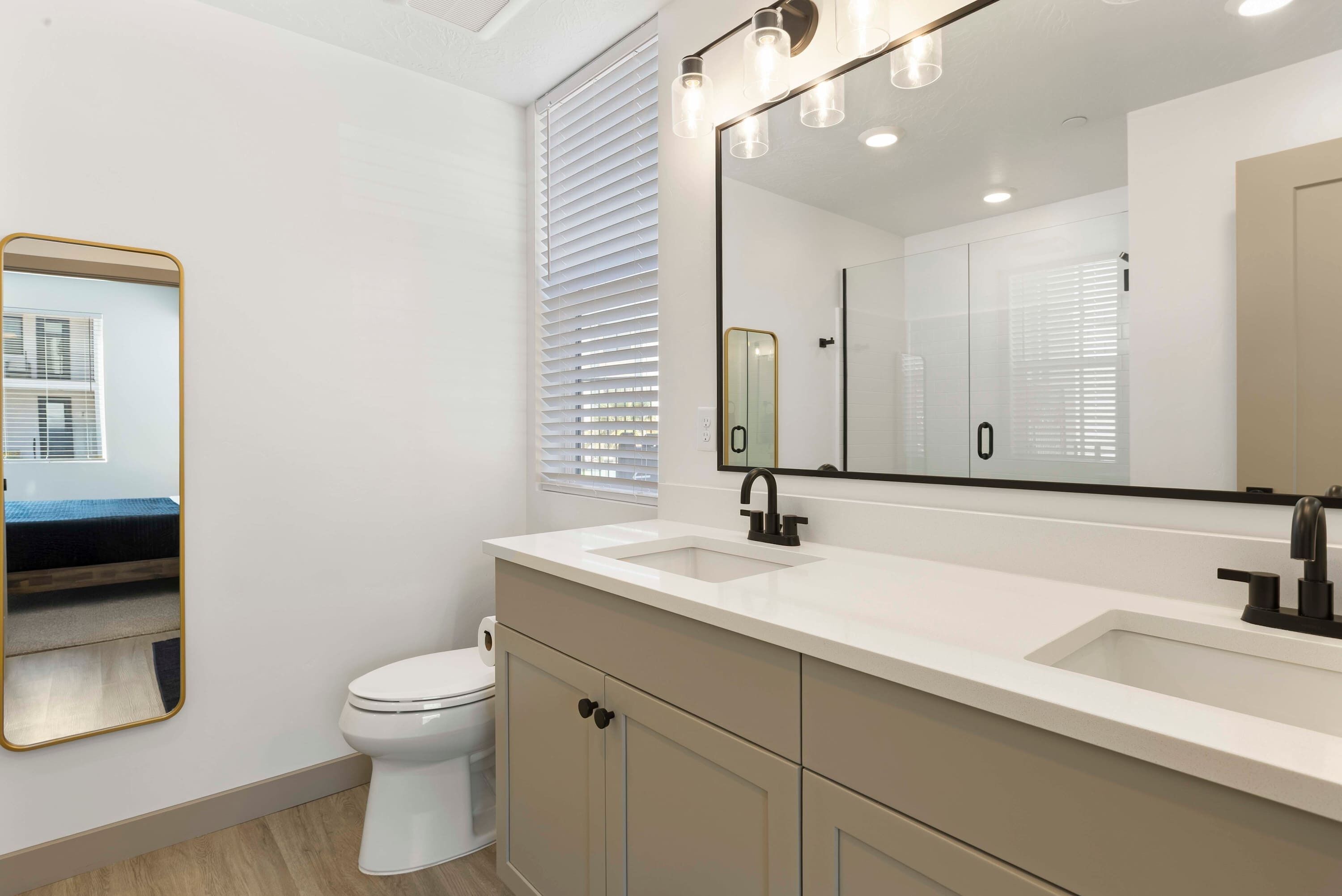 A modern bathroom with a white toilet, a large mirror, and a vanity with a sink.