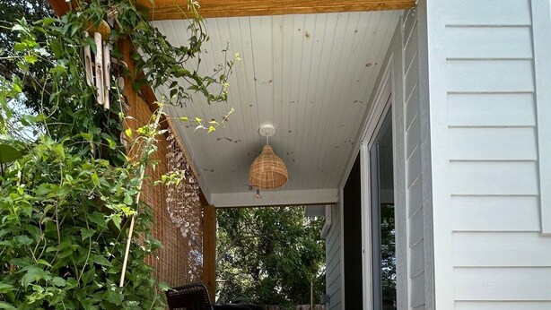 Une terrasse en bois avec un banc, un luminaire suspendu et un paillasson avec du texte.