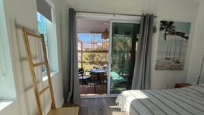 Une chambre à coucher comprenant un lit, une chaise en bois, une fenêtre et un balcon aménagé avec du mobilier d’extérieur.