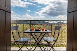 A balcony with a table set for two, a metal railing, and a view of the countryside. - Livadi Loft | Cozy Getaway in Parnassos (Kalyvia Livadiou Arachovas)