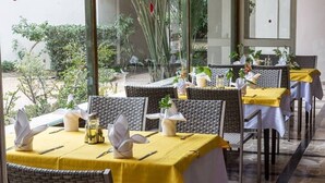 A restaurant with outdoor seating, wicker chairs, yellow tablecloths, and potted plants.