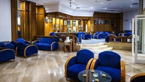 A hotel lobby with blue upholstered seating, a bar area, and a staircase leading to an upper level.