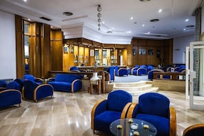 Eine Hotelhalle mit blau gepolsterten Sitzgelegenheiten, einer Bar und einer Treppe zu einer oberen Ebene.