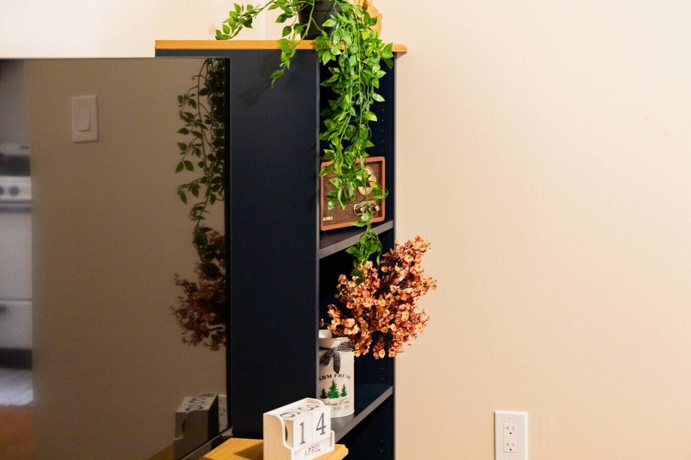 A room with a black shelving unit, a small plant, and a calendar indicating April 14th.