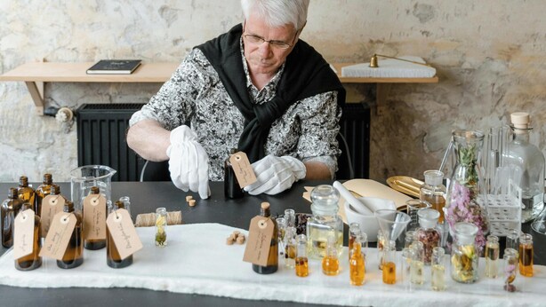Una persona organizando botellas sobre una mesa en una habitación con pared de mármol y luminarias fijadas a la pared.