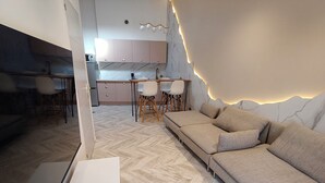 Una sala moderna con sofá, suelo con motivo de espiga y cocina al fondo.