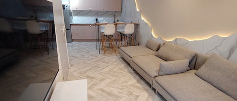 A modern living room with a sofa, herringbone-patterned floor, and a kitchen in the background.