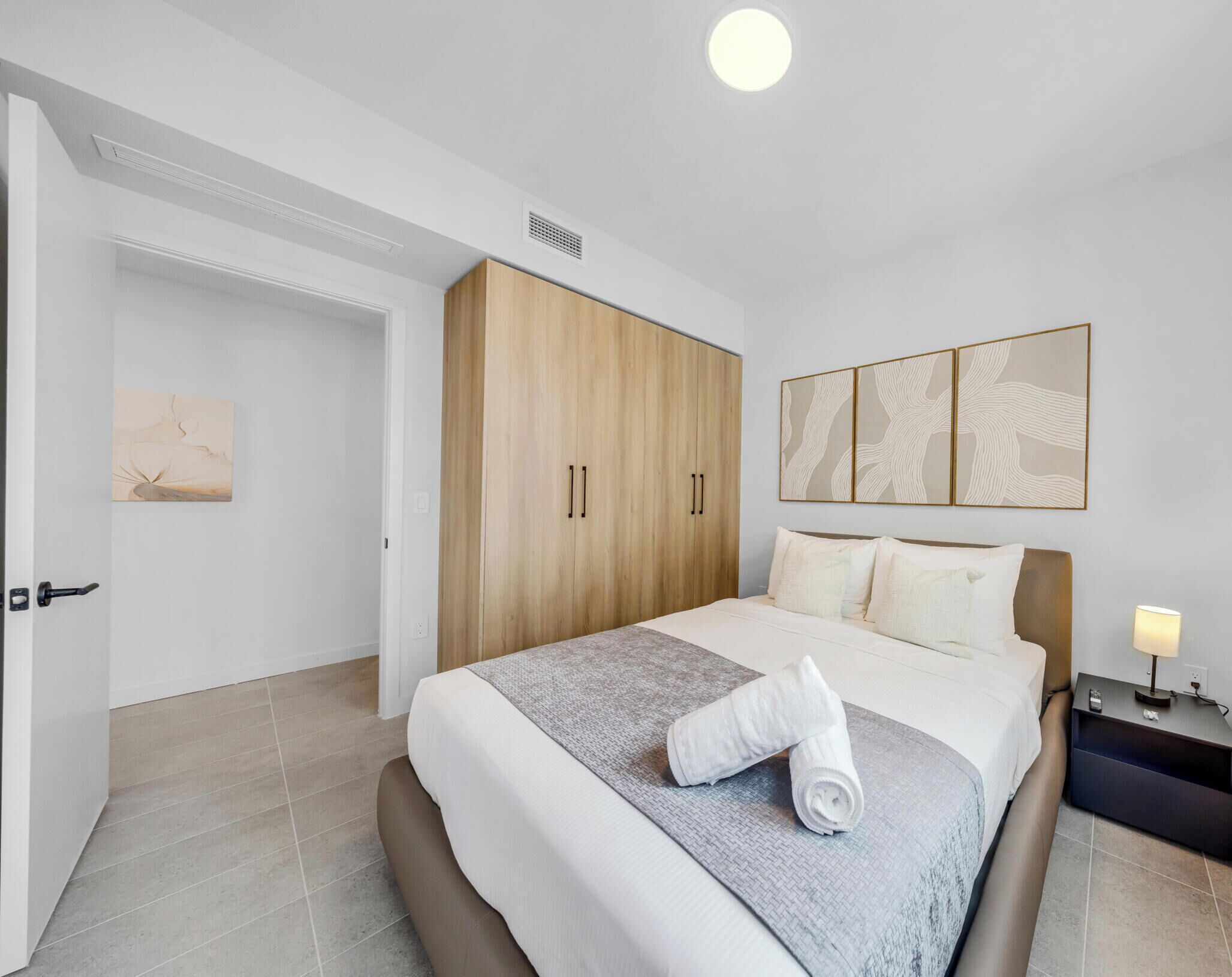 Una camera da letto con un letto, un armadio, un comodino, una lampada e un quadro appeso alla parete.