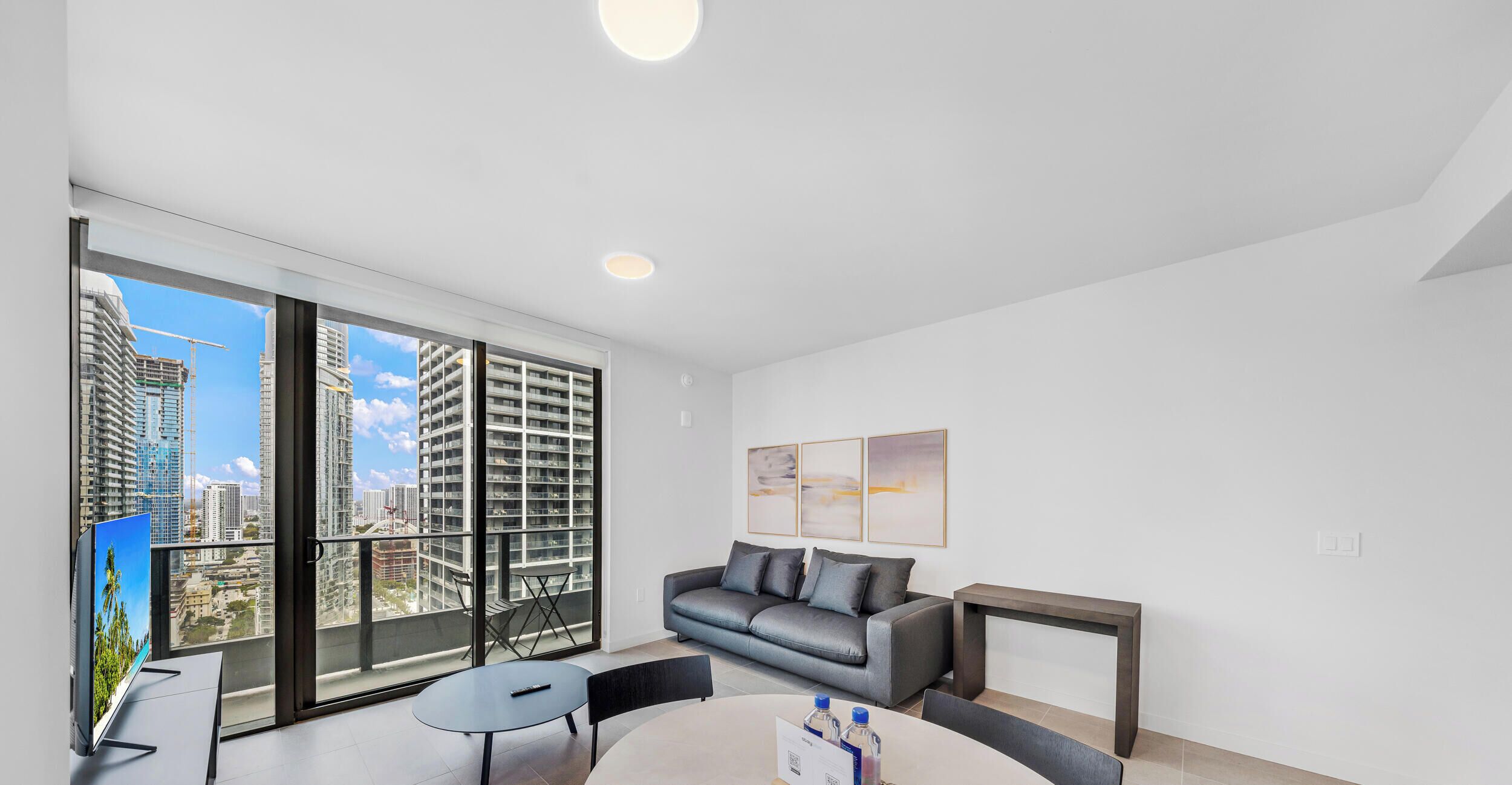 A modern living room with a large window, a sofa, a coffee table, and a flat-screen TV.
