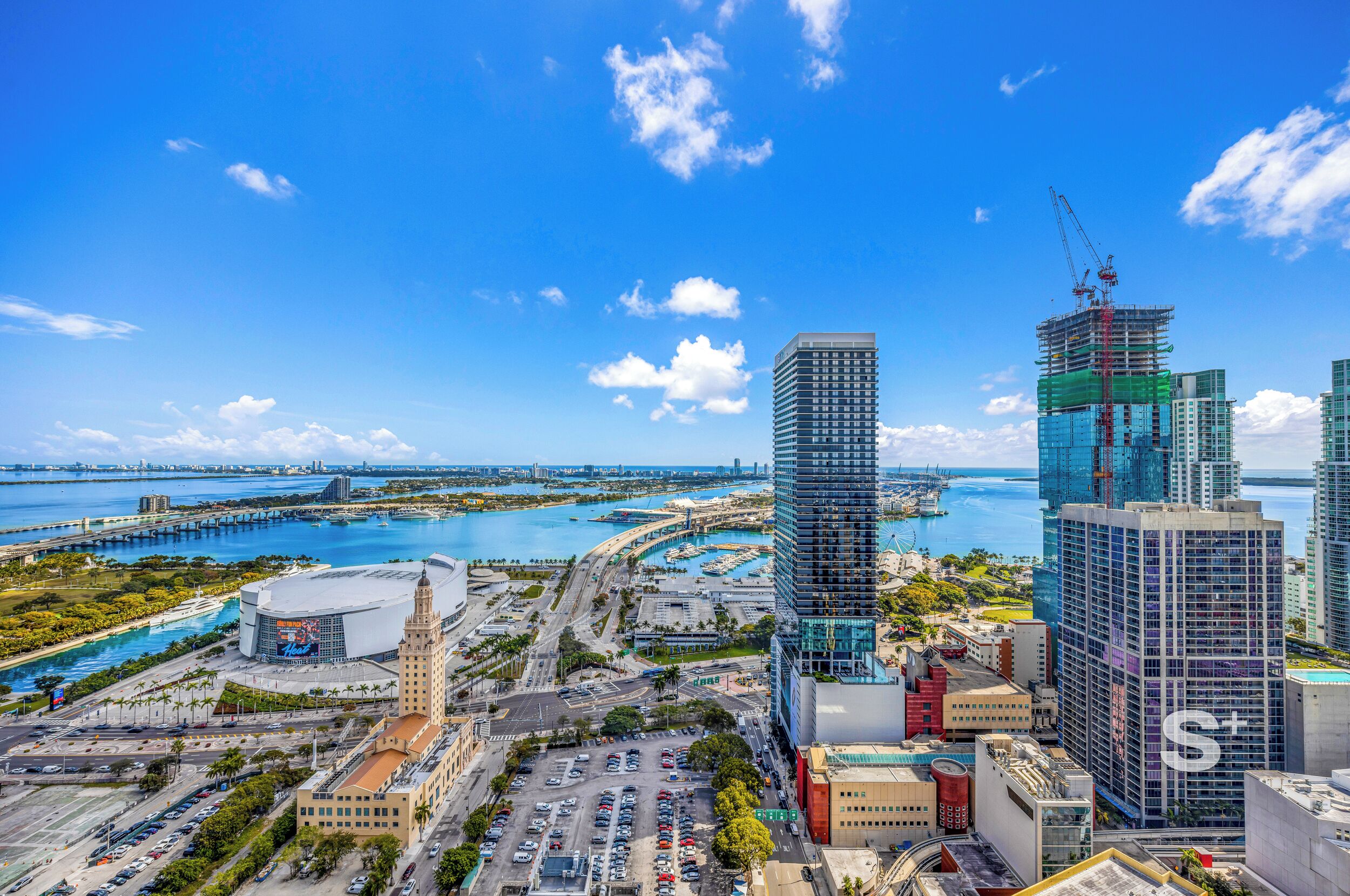 A cityscape with modern high-rise buildings, a marina, and a large stadium.