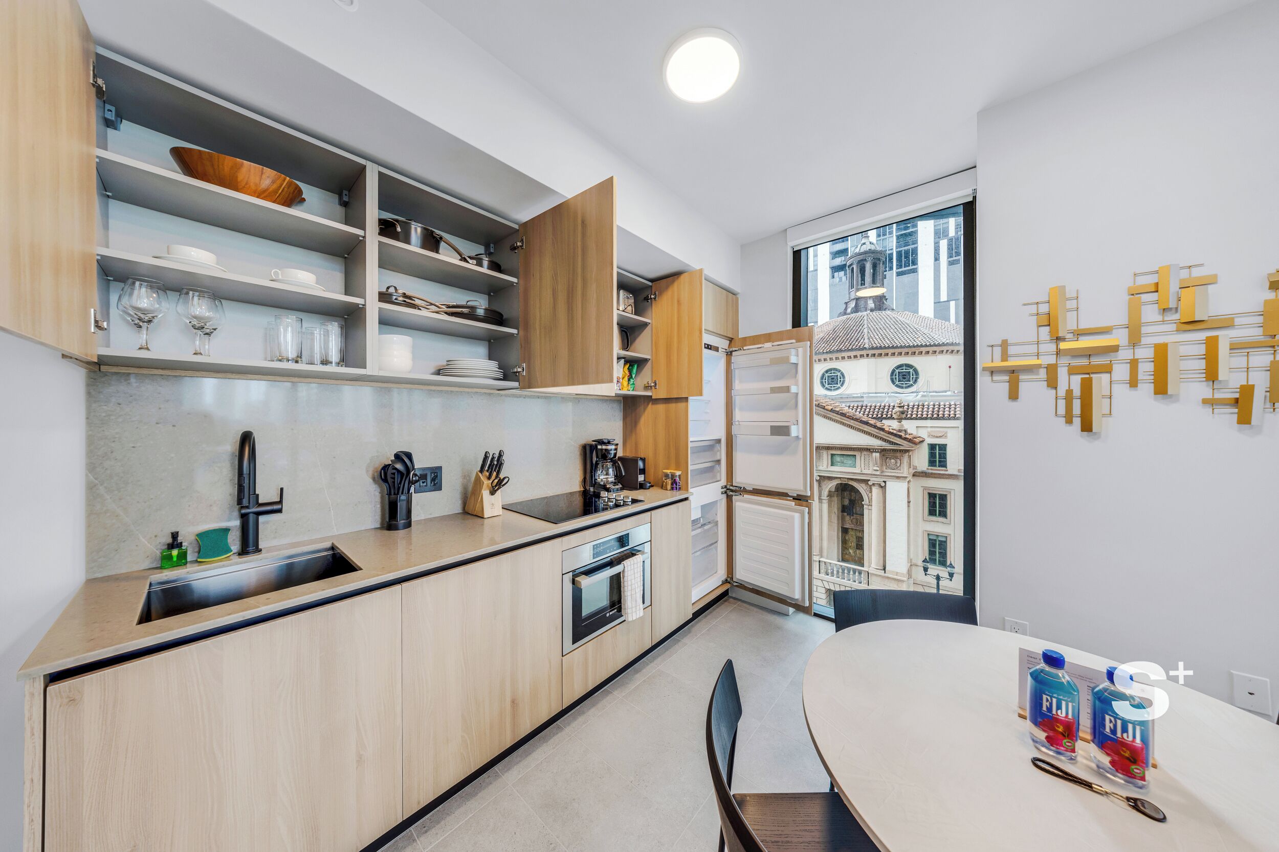 A modern kitchen with built-in appliances, a dining area with a table, and a view of a historic building through a large window.