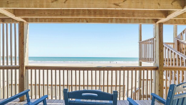 Eine Holzterrasse mit Blick auf Strand und Meer.