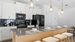 A modern kitchen with white cabinets, stainless steel appliances, a central island with stools, and pendant lighting. - Chic Family Retreat, Pool, Mario and Mickey Rooms (Davenport)