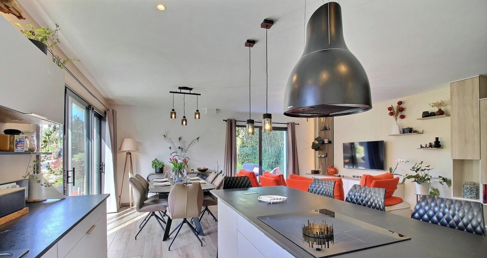 A modern kitchen with a central island, pendant lighting, and a dining area with orange chairs.