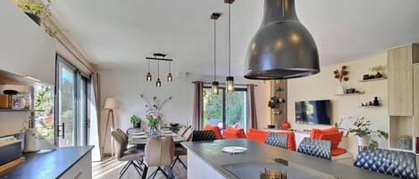 A modern kitchen with a central island, pendant lighting, and a dining area with orange chairs.