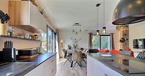 A modern kitchen with a central island, pendant lighting, and a dining area with chairs and a table. - Balizenn - SAINT PIERRE QUIBERON (SAINT PIERRE QUIBERON)