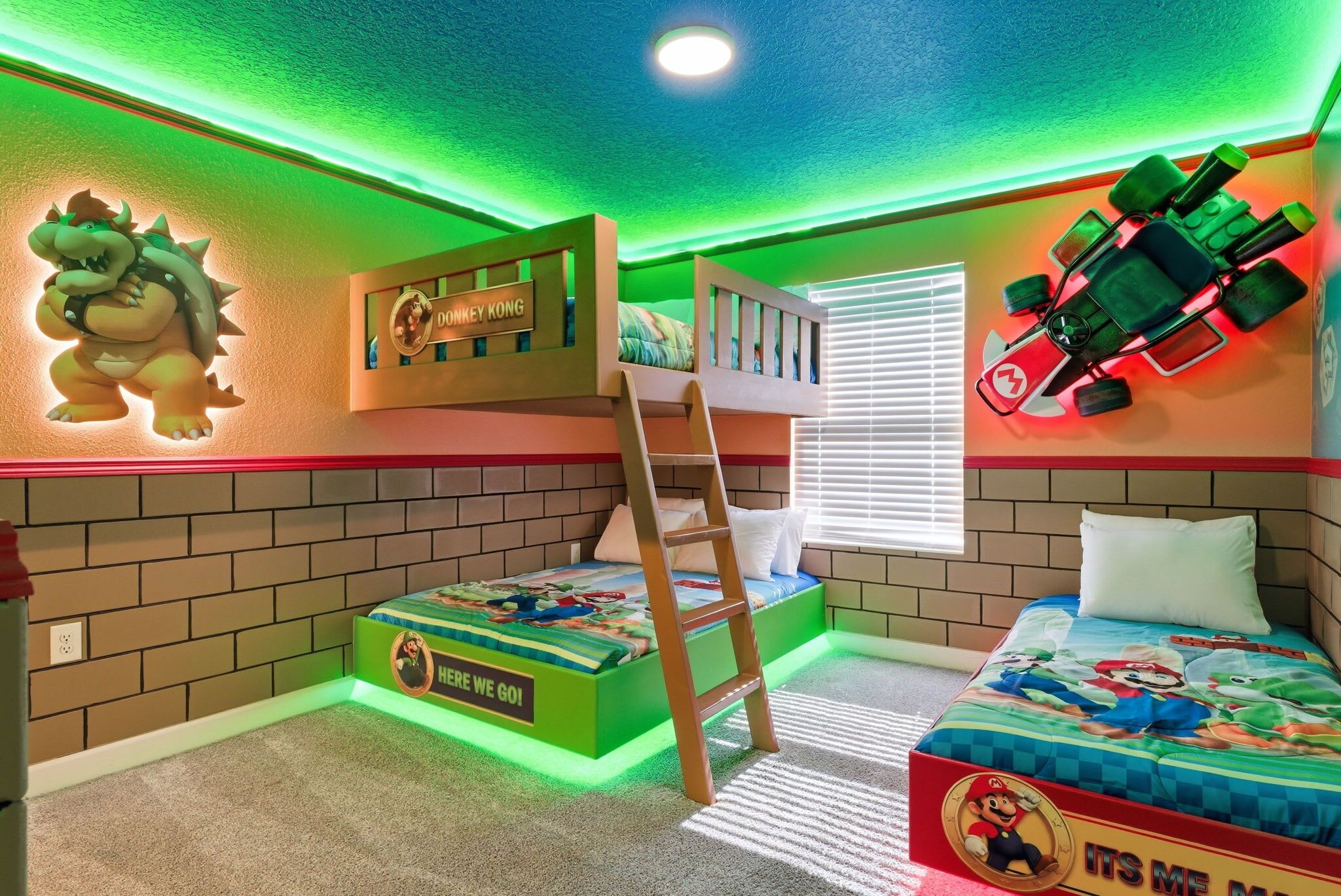 Habitación infantil con una cama litera, una escalera, una colcha con tema de Mario, alfombra verde y una pared con un personaje de caricatura.