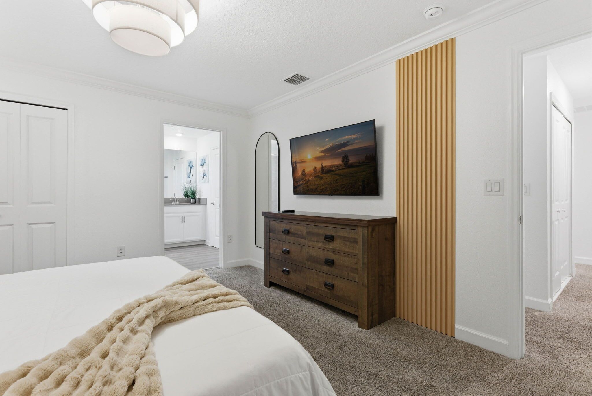A bedroom with a bed, a dresser, a painting, and a hallway leading to a bathroom.