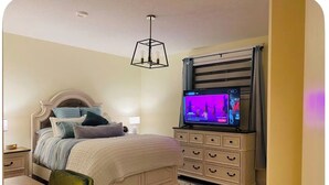 Ein Schlafzimmer mit Bett, Nachttisch, Lampe, Kommode, Fernseher und einer Pendelleuchte.