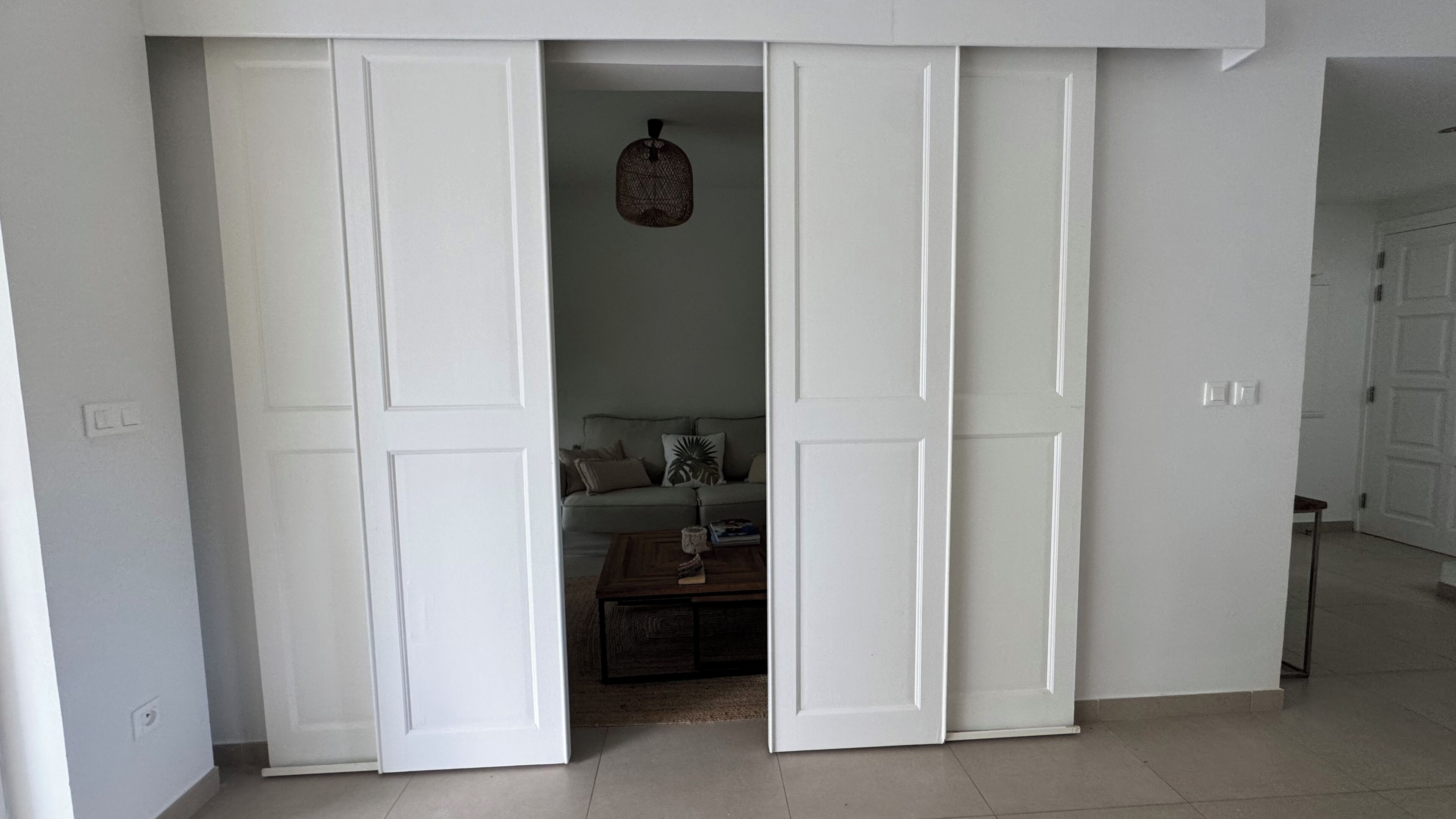 A room with a large white door, a small table with books, and a sofa with cushions.