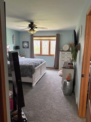 Une chambre à coucher avec un lit, une commode, une coiffeuse et une fenêtre avec des rideaux.