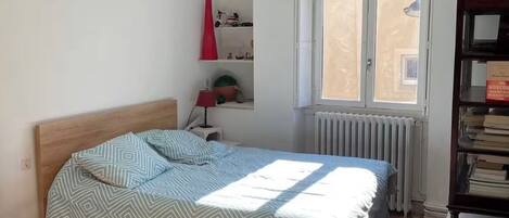 A bedroom with a bed, a radiator, a window, and a ceiling fan.