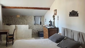 Une chambre à coucher avec un lit, un bureau, une chaise, une commode et un mur en pierre.