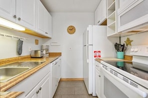 Een kleine keuken met witte kasten, een klok aan de muur, een broodrooster en een koelkast.