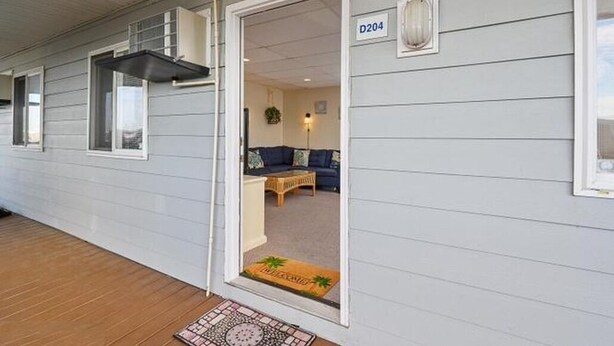 A single-story building with a covered porch, a door marked 'D204,' and a living room with a sofa and a coffee table. - Cozy bayside 2BR 1BA condo;pool,private parking,WIFI;beach/boardwalk-10 min walk (Ocean City)