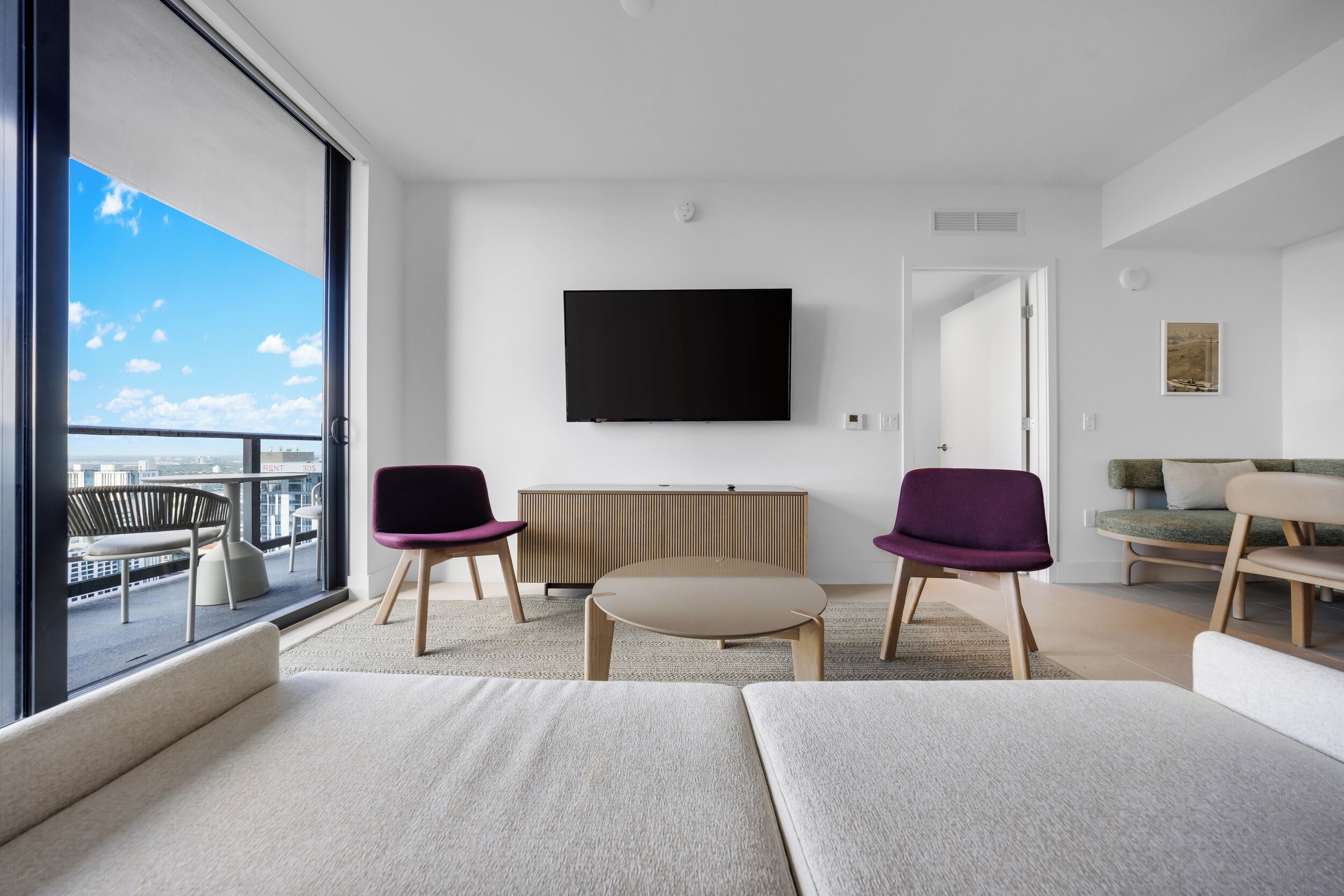 Un salon moderne doté d’une grande fenêtre, d’un téléviseur à écran plat et offrant une vue sur la ville.