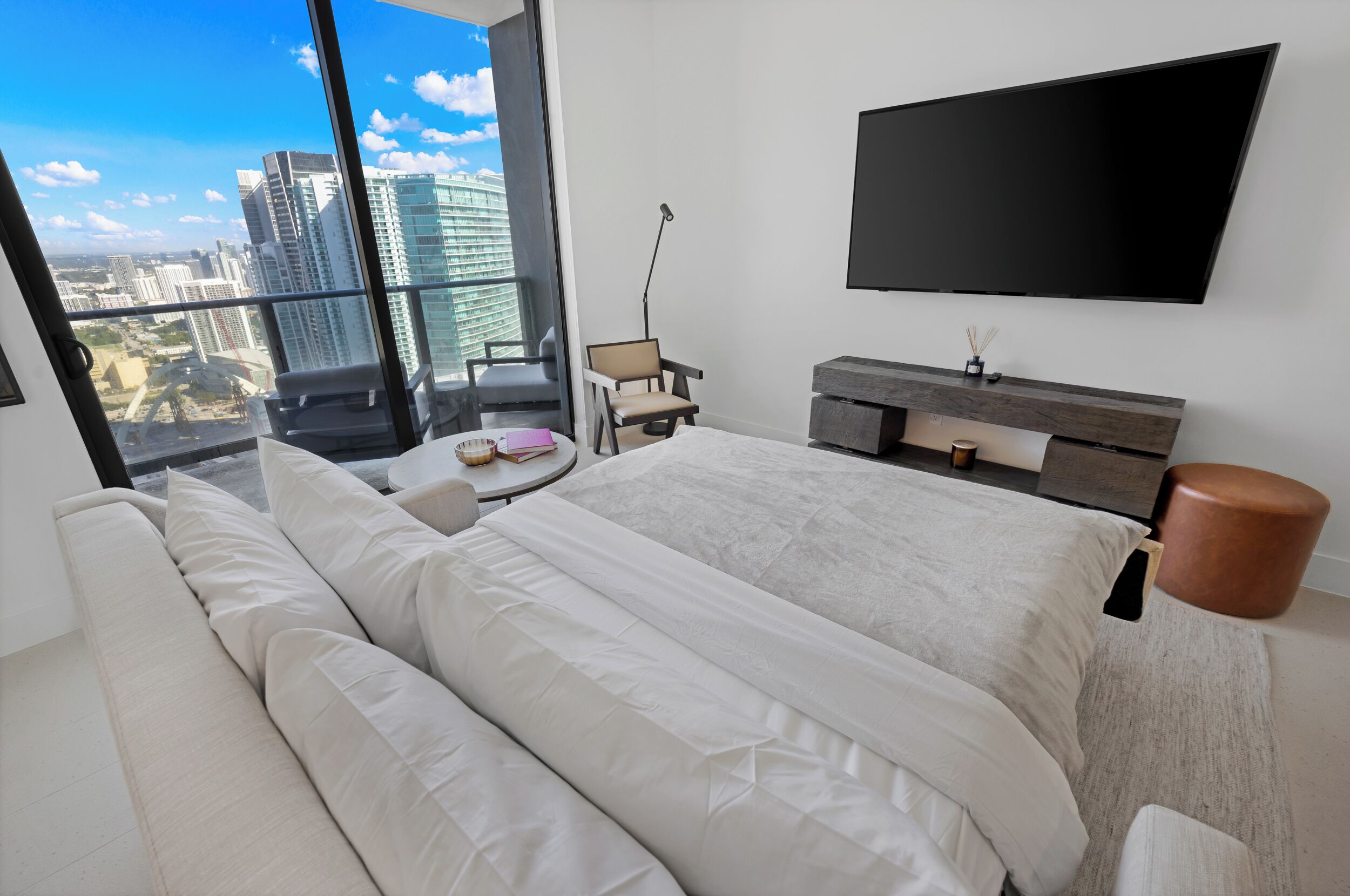 Une chambre d’hôtel moderne, dotée d’un grand lit, d’un canapé, d’une télévision et offrant une vue sur les bâtiments de la ville.