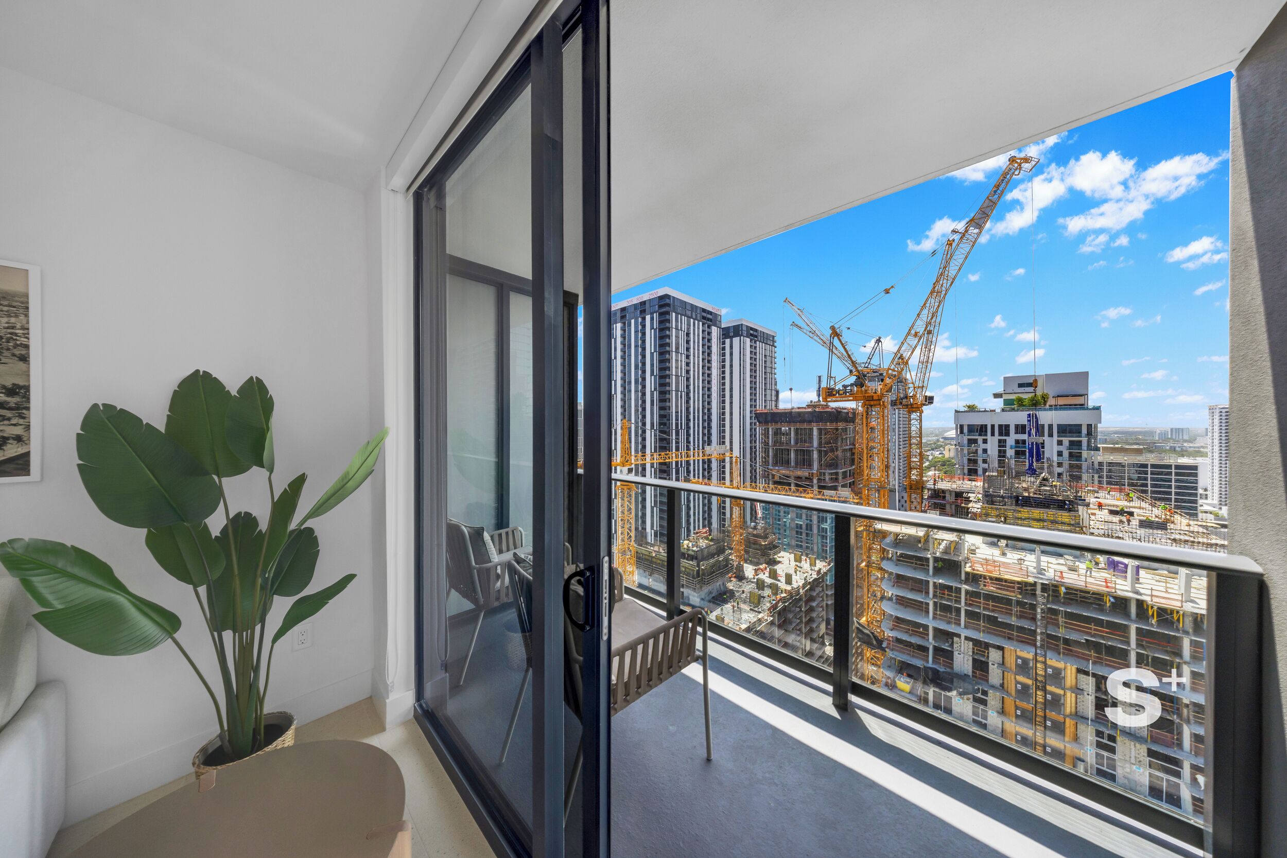 A balcony with a view of a construction site, a potted plant, and a chair.