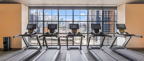 Une salle de sport équipée de tapis de course, d’écrans pour les exercices et offrant une vue sur la ville grâce à de grandes fenêtres.