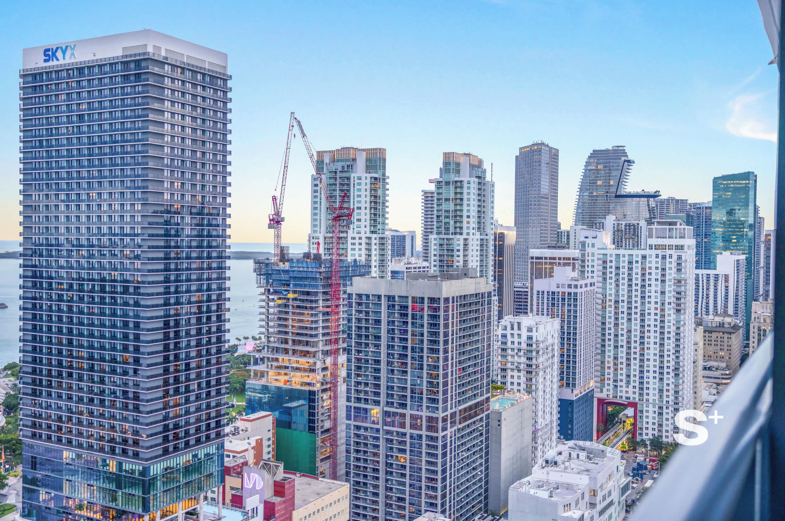 A high-rise building with a prominent 'SKYY' sign, surrounded by other tall buildings and construction cranes.