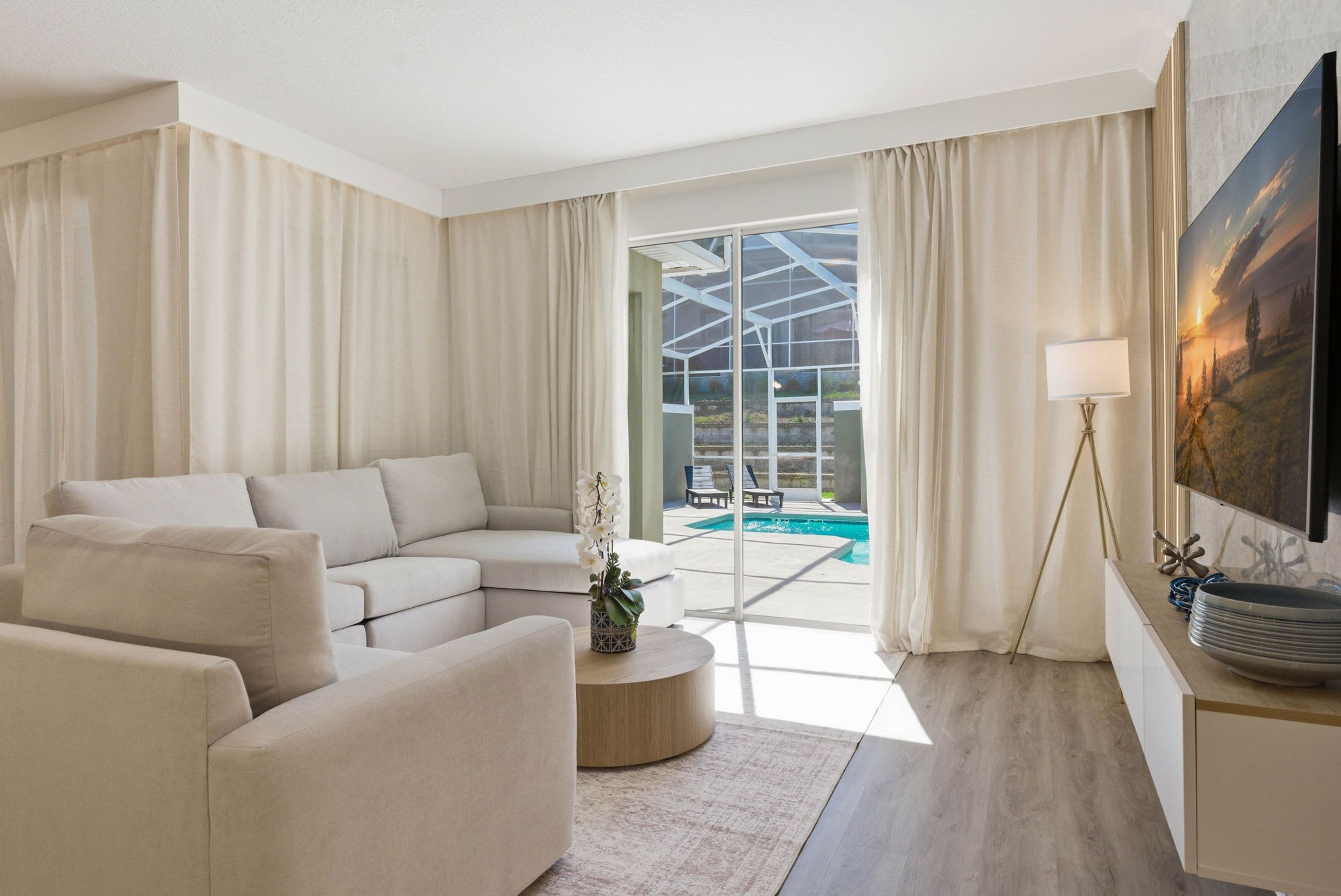 Una sala de estar moderna con un sofá modular, una mesa de centro, un televisor y vistas a una piscina y zona exterior.