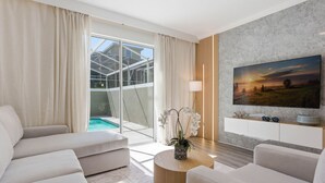 A modern living room with a sofa, a coffee table, a TV, and a view of a swimming pool. - Chic Family Retreat Pool Mario and Mickey Rooms (Davenport)