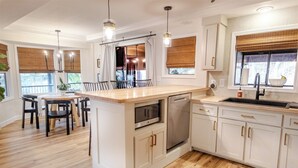 Una cocina moderna con una isla central, muebles blancos y un comedor con sillas.