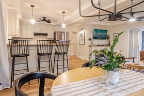 Una cocina moderna con armarios blancos, un refrigerador de acero inoxidable y un comedor con una mesa de madera y sillas negras.