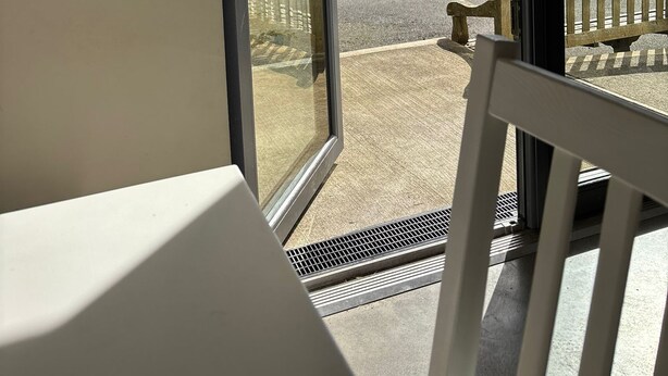 A view from a room with a sliding glass door, leading to a balcony with a bench and a view of a body of water and buildings. - Guest house overlooking Lough Conn (Foxford)