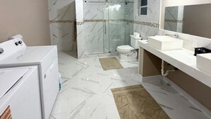 Casa de banho com máquina de lavar roupa, chuveiro com portas de vidro, sanita e lavatório com espelho.