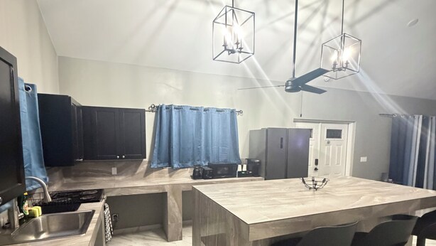 Cozinha moderna com ilha central, banquetas, ventilador de teto e luminárias pendentes.