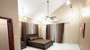 Quarto com cama, cortinas, ventoinha no teto e luminária.